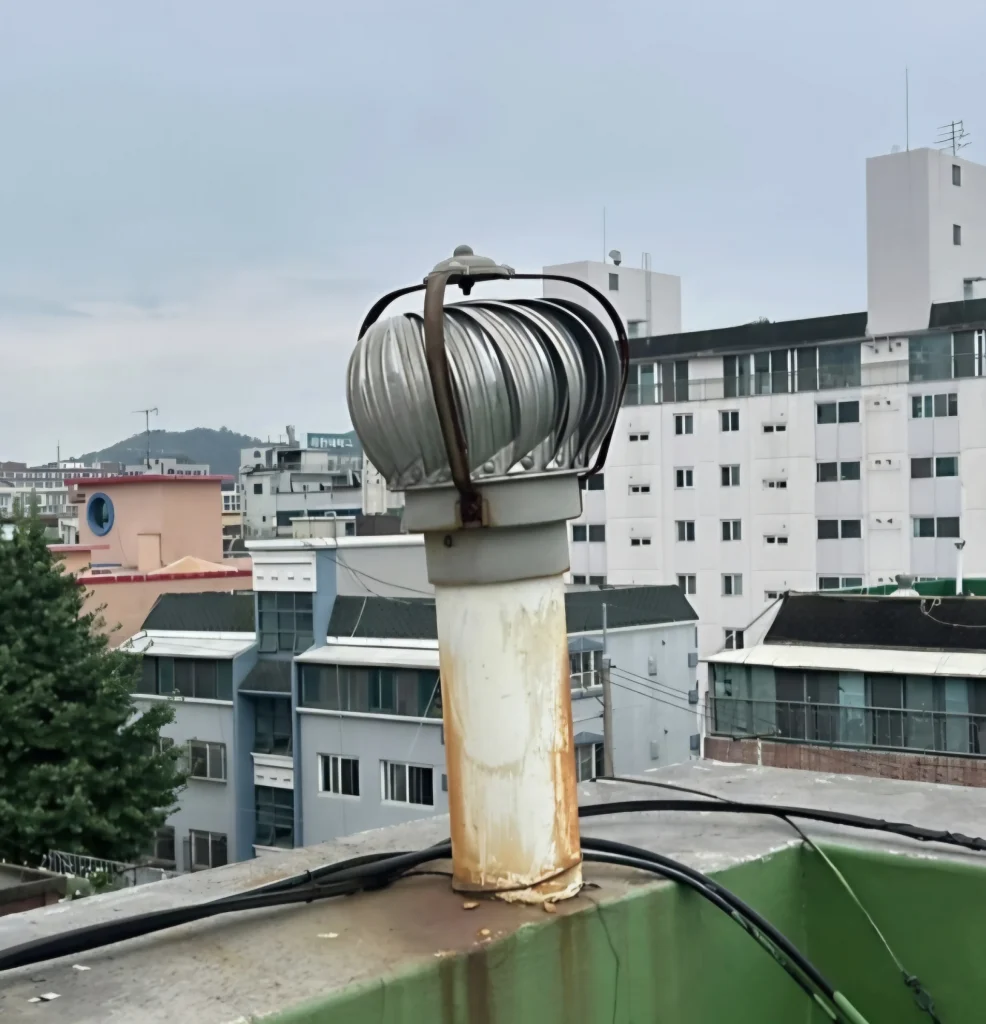 옥상 환기구에 낡은 환풍기가 부식된 채 설치된 모습